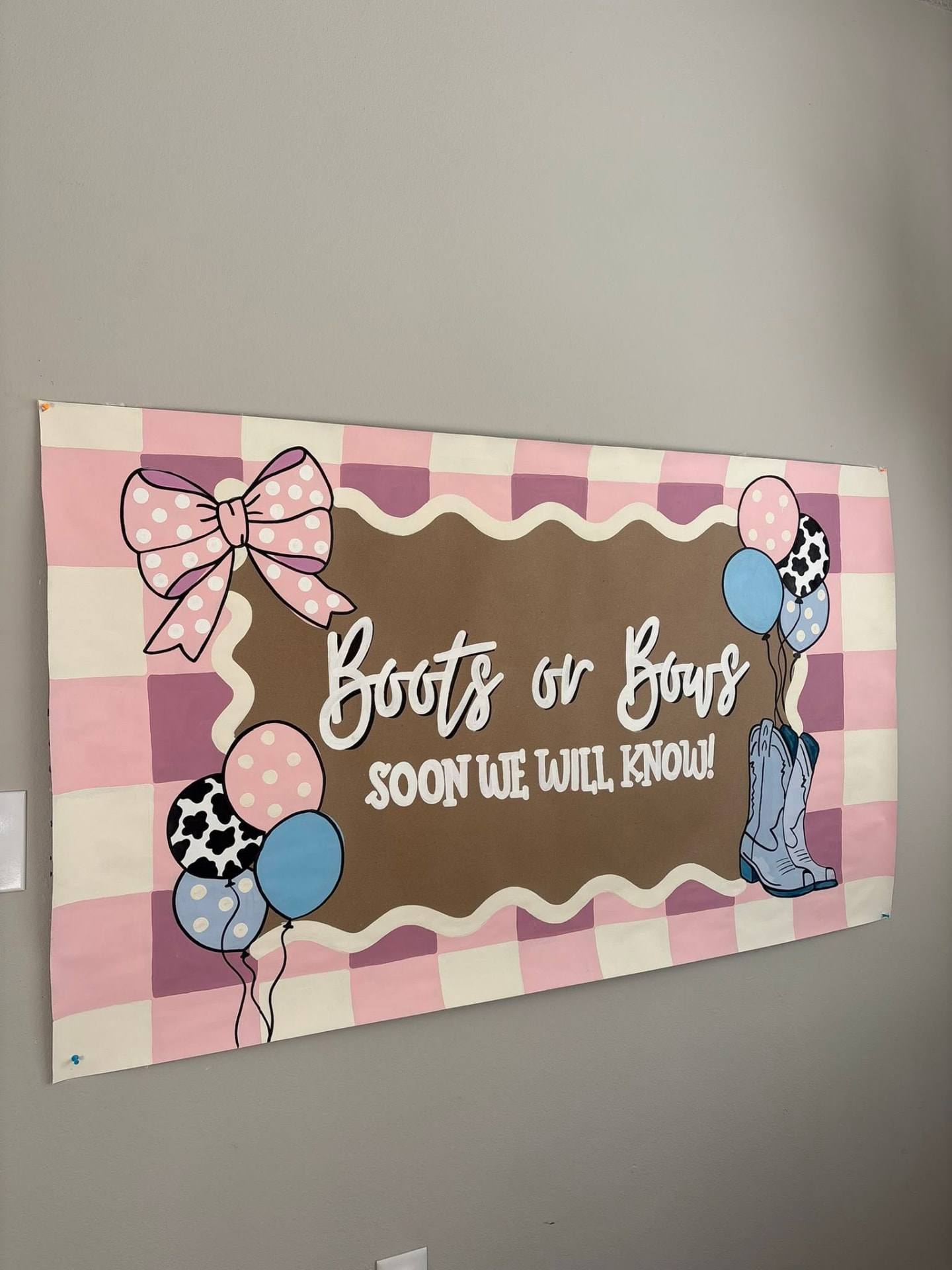 Pink and lilac checkerboard gender reveal banner with bows, balloons, and cowboy boots